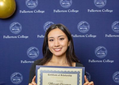 A person holds a scholarship certificate in front of a blue backdrop featuring the Fullerton College logo and balloons.