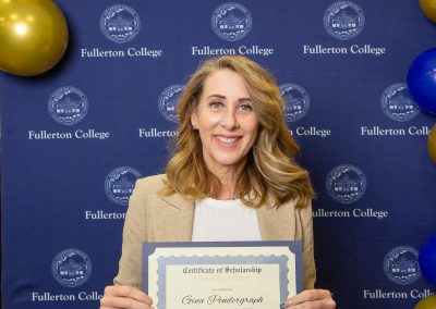 A person holds a scholarship certificate in front of a backdrop featuring the Fullerton College logo and blue and gold balloons.