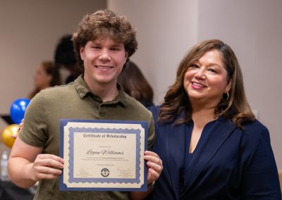 A young person and an adult stand together, smiling as they hold up a certificate of scholarship.