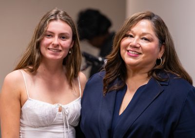 Two individuals smile warmly at the camera in a well-lit indoor setting.