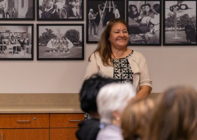 A person stands smiling in front of an audience, with a wall behind them displaying framed black-and-white photographs.