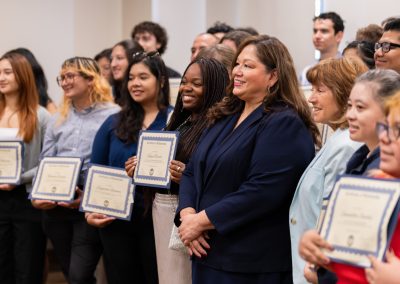 A group of individuals stand together, smiling and holding certificates of recognition.