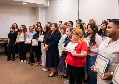 A group of individuals stand in a line indoors, each holding a framed certificate, during what appears to be an awards ceremony.