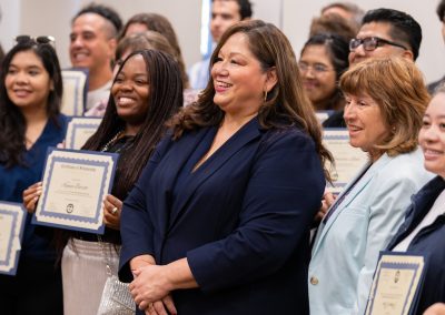 A group of individuals in formal attire stand together, smiling and holding certificates of recognition.