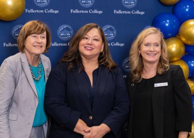 Three individuals pose together at a Fullerton College event, standing before a branded backdrop adorned with blue and gold balloons.