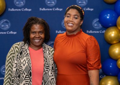 Two individuals smile for a photo at a Fullerton College event, with blue and gold balloons in the background.