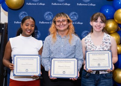 Three individuals stand together at a Fuller College event, each holding a Certificate of Scholarship, with blue and gold balloons decorating the background.